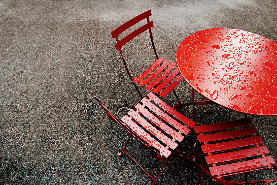 Regentropfen auf dem roten Metalltisch und den Stühlen