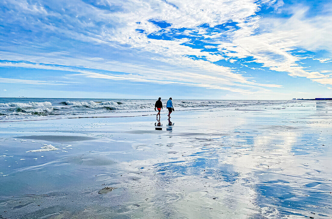 Two people strolling on a beach at low tide.