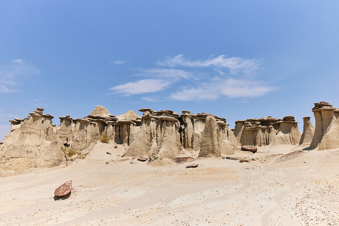 Low angle wide shot of sandstone hoodoos and a clear blue sky at Ah-shi-sle-pah Wilderness Study Area in New Mexico. Area is located in northwestern New Mexico and is a badland area of rolling water-carved clay hills. It is a landscape of sandstone cap rocks and scenic olive-colored hills. Water in this area is scarce and there are no trails; however, the area is scenic and contains soft colors rarely seen elsewhere