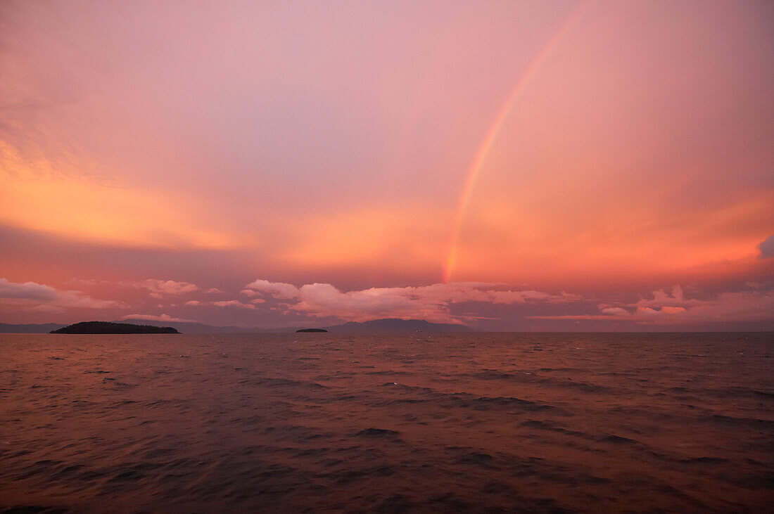 Looking across sea at pink sky, islands and rainbow at sunset in the Verde Island Passage between Batangas and Sabang Beach, Philippines