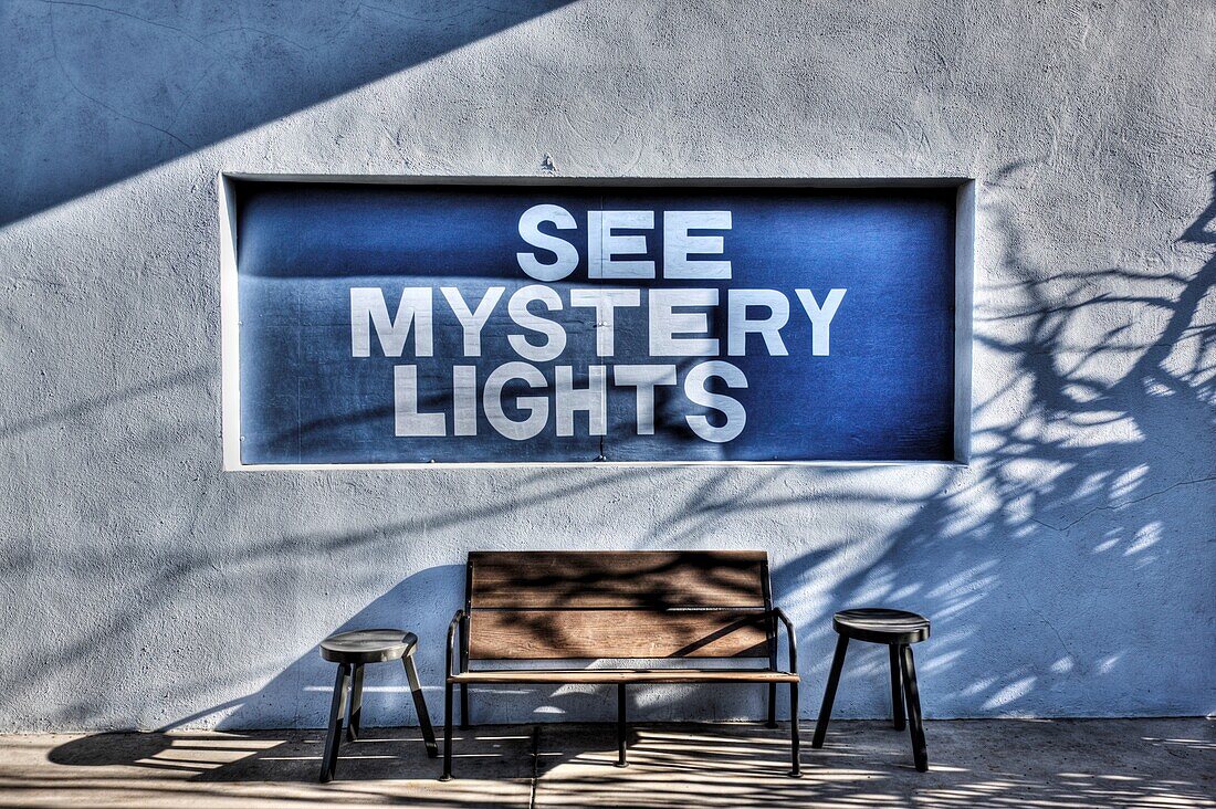 See Mystery Lights sign on a building with a bench and two stools, Marfa, Texas, USA
