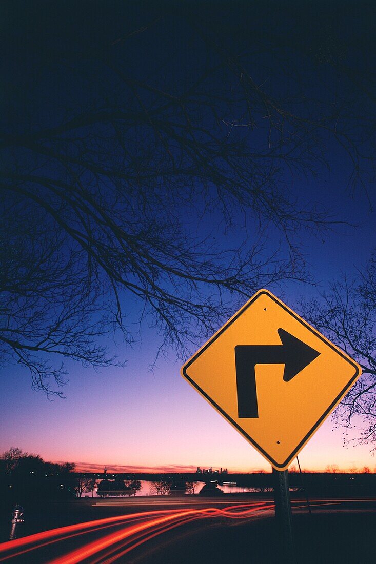 Neonstreifen des Verkehrs und ein Schild mit Richtungspfeil nach rechts am Straßenrand in der Nähe eines Sees, White Rock Lake, Dallas, Texas, USA