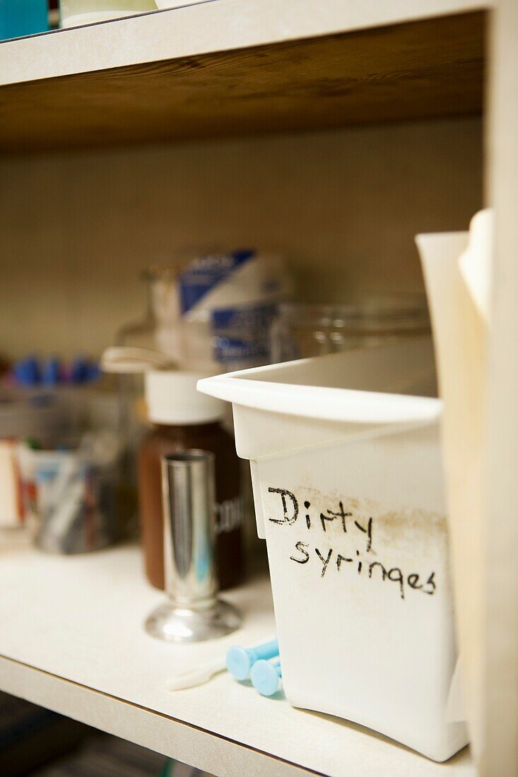 Plastic container labeled dirty syringes on a shelf at a clinic