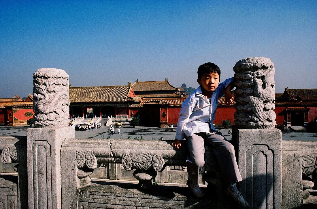 Junge sitzt auf der steinernen Barrikade mit einem Palast im Hintergrund, Imperial Palace, Verbotene Stadt, Peking, China