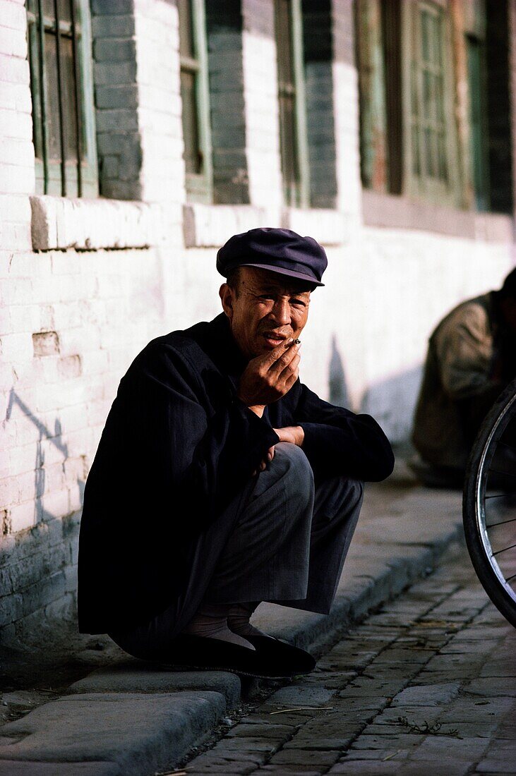 Man smoking a cigarette while squatting on the sidewalk, China