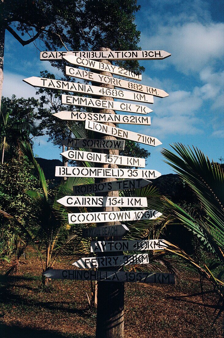 Directional signs posted to a pole surrounded by lush plants, Port Douglas, Queensland, Australia