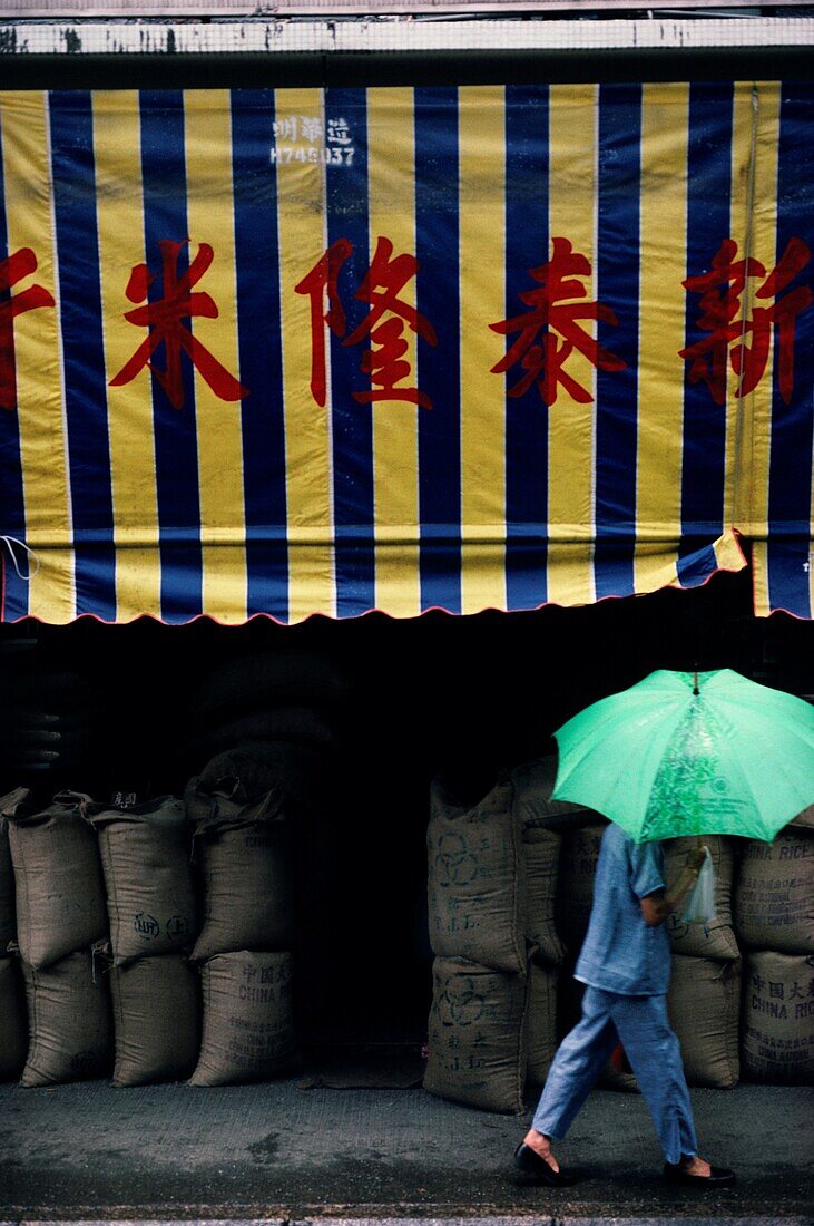 Woman carrying an umbrella walking past rice market, Hong Kong