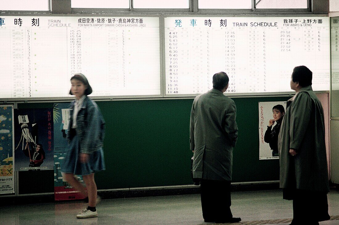 Woman walking away from train schedule as two men check schedule, Tokyo, Japan