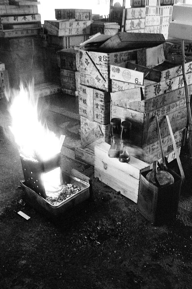 Japan, Tokyo, Fire burning in furnace next to pair of boots and wooden shipping crates inside Tsukiji fish market