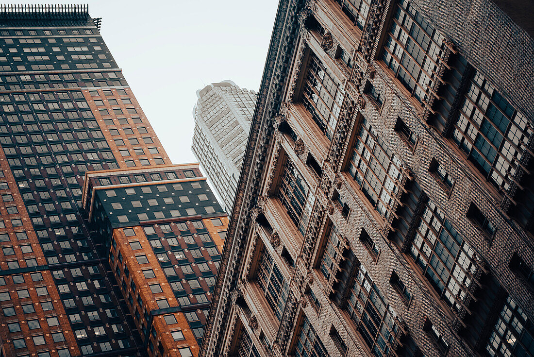 Zwei gemauerte Hochhäuser in Manhattan vor einem Wolkenkratzer an einem nebligen Morgen.