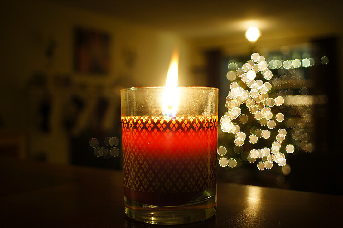 Christmas candle burning with a long flame in front of an out of focus Christmas tree.