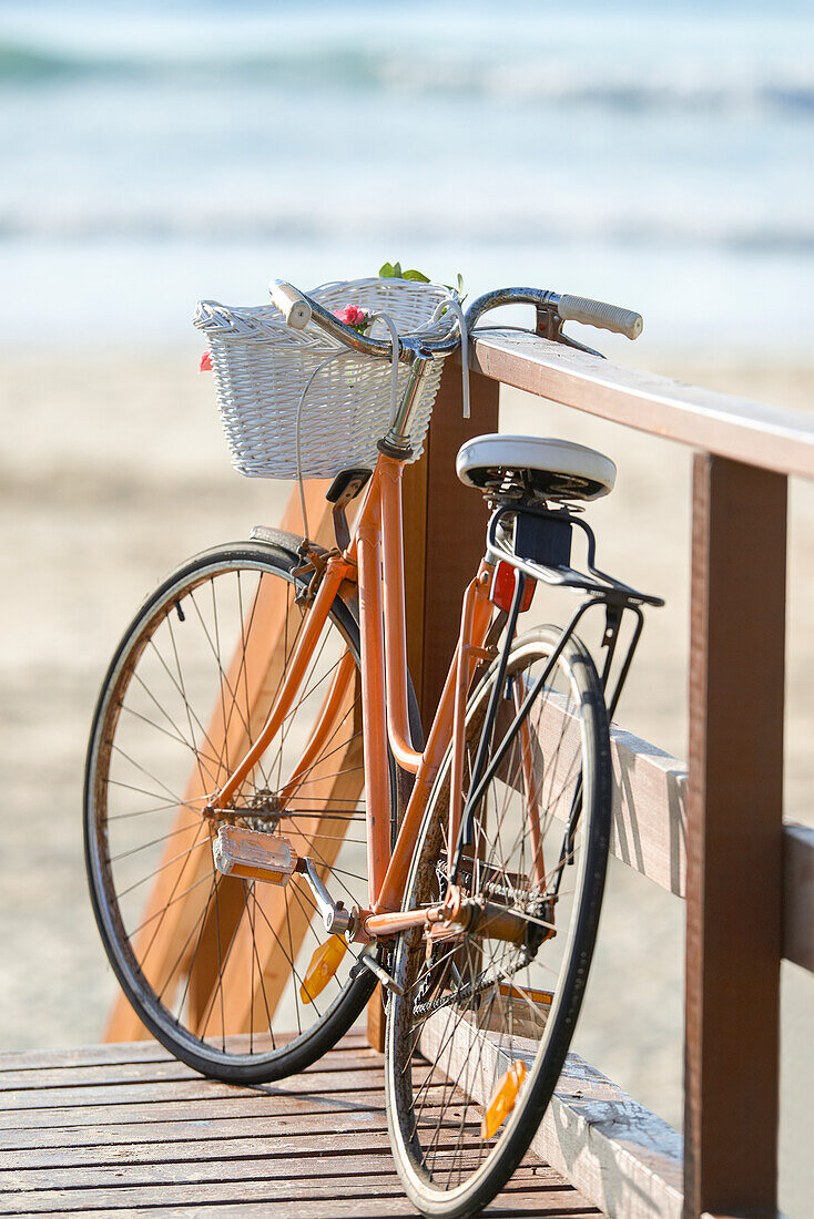 Nahaufnahme des Fahrrads der Frau, das sich am Strand an das Geländer lehnt
