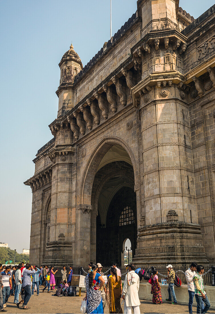 People standing next to the Gateway of India stone arch situated on the shore of the Arabian Sea. Completed in 1924 and built to commemorate the landing of King George V.
