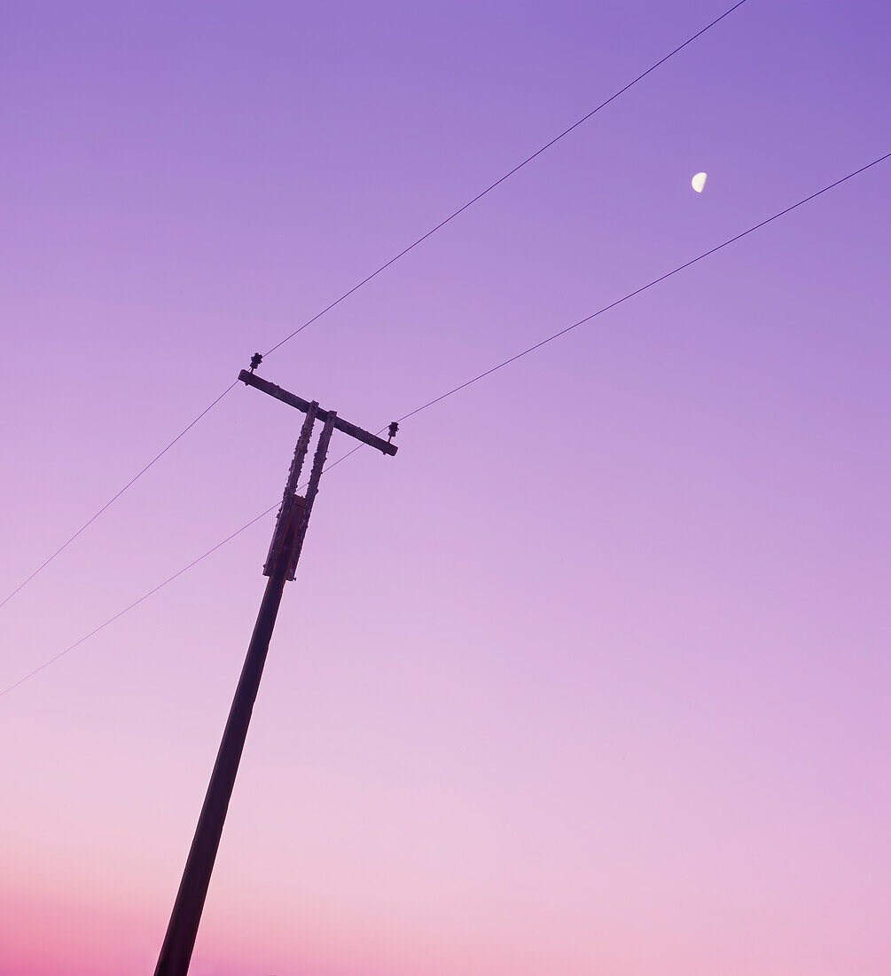 Telefonmast gegen rosafarbenen Himmel und Mond im Himmel