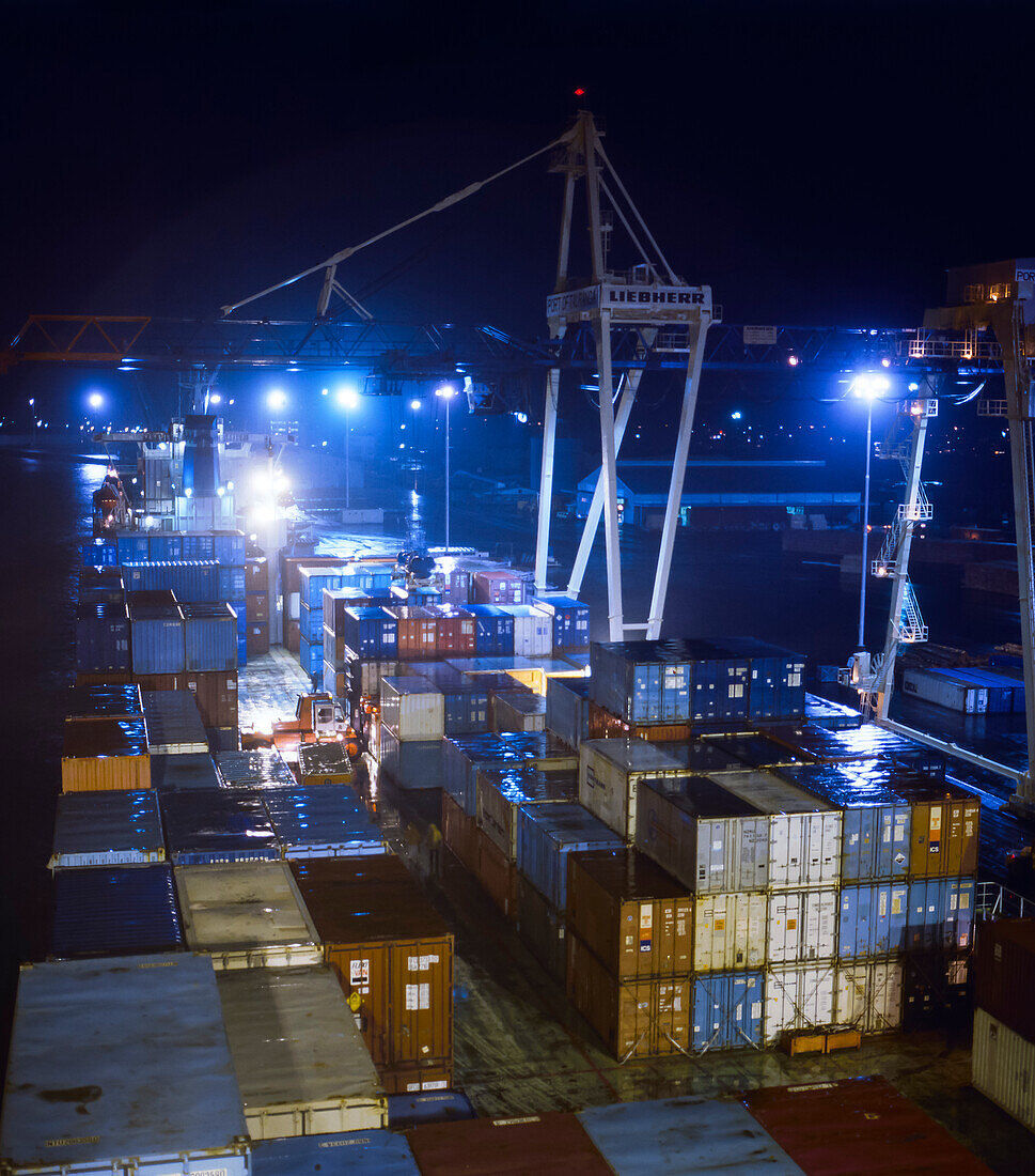 Crane unloading ship's containers onto wharf at night