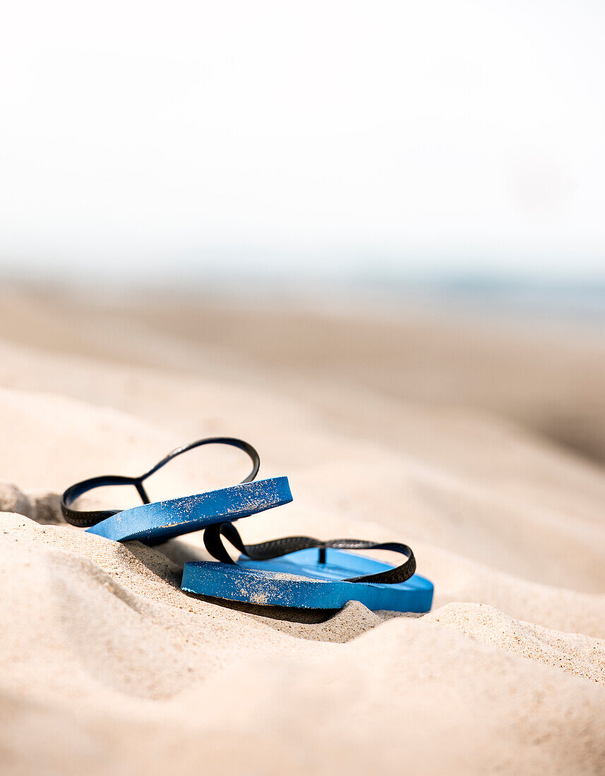 Blaues Paar Flip-Flops auf dem Sand verlassen