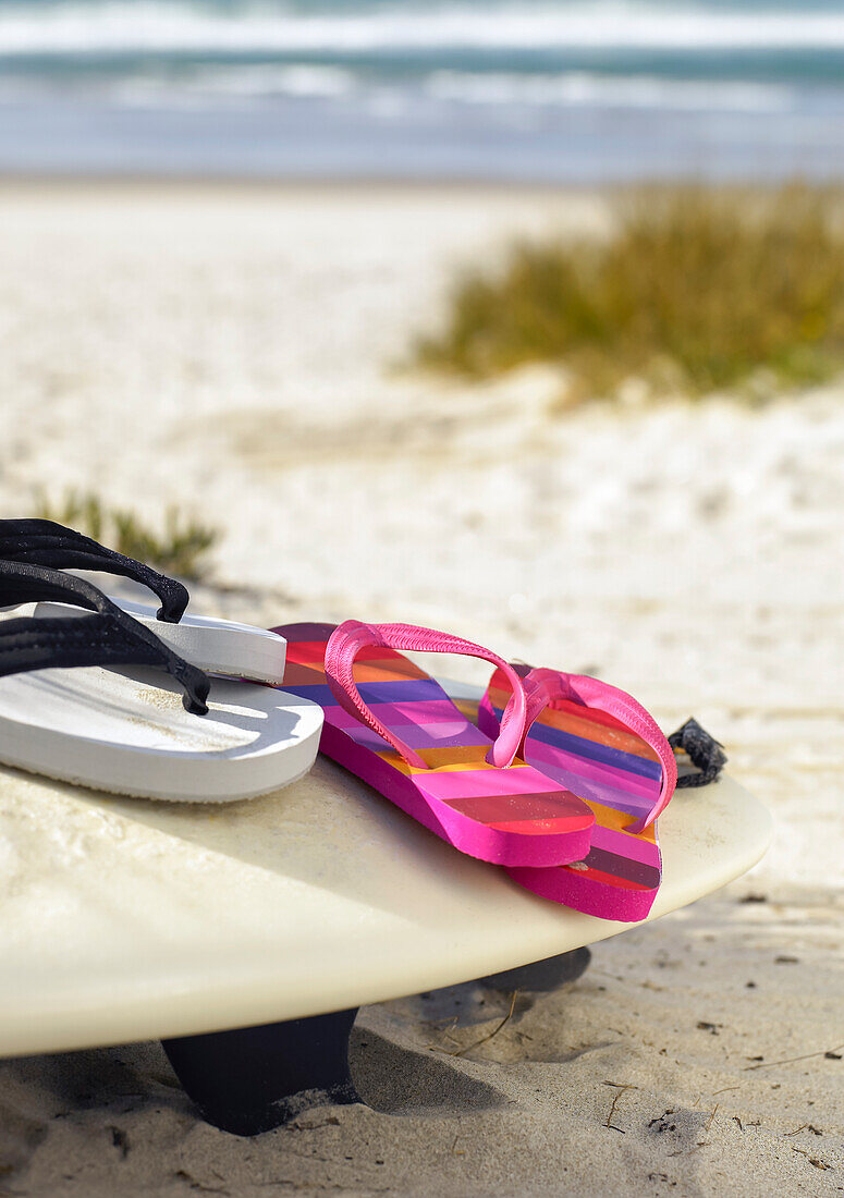 Flip flops resting on surfboard in the sand