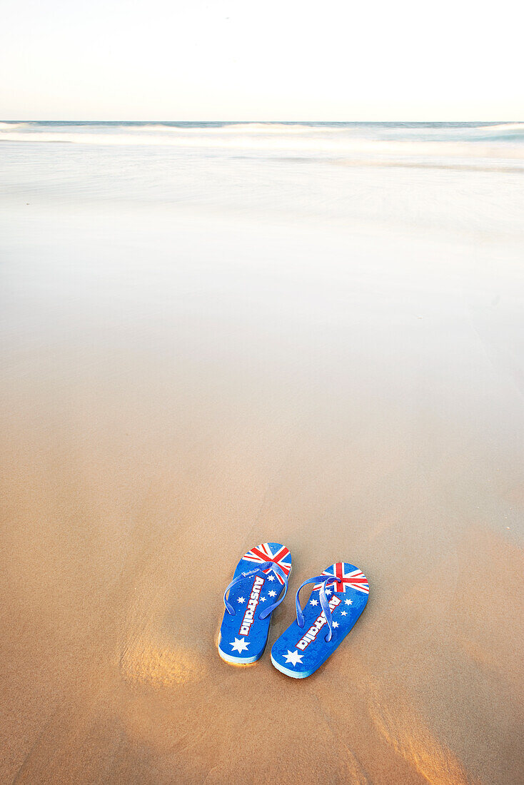 Jandals, Riemen, mit australischer Flagge auf dem Sand mit Wellen im Hintergrund