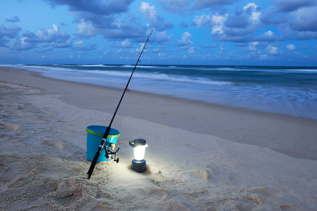 Angelrute, Eimer und Lampe auf dem Sand am Meer - früher Abend