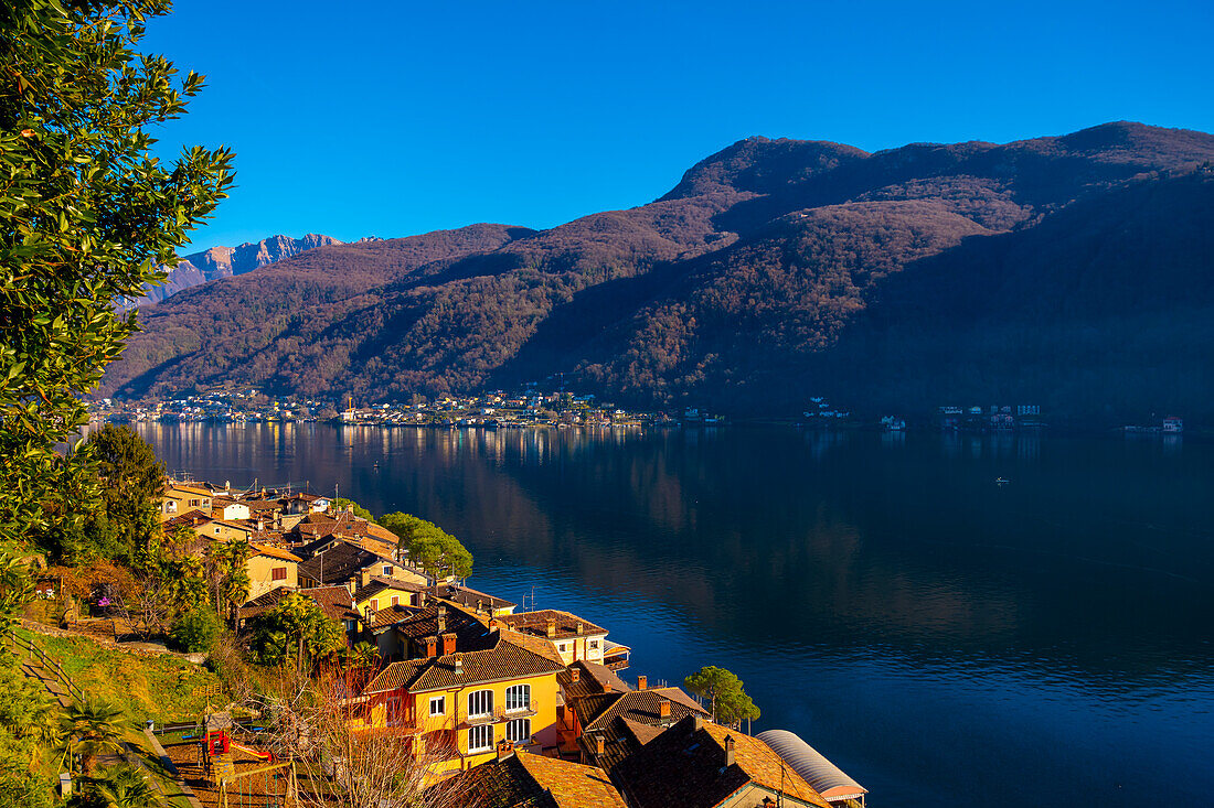 Stadtbild und Luganersee mit blauem Himmel und Berg an einem sonnigen Tag in Morcote, Tessin in der Schweiz