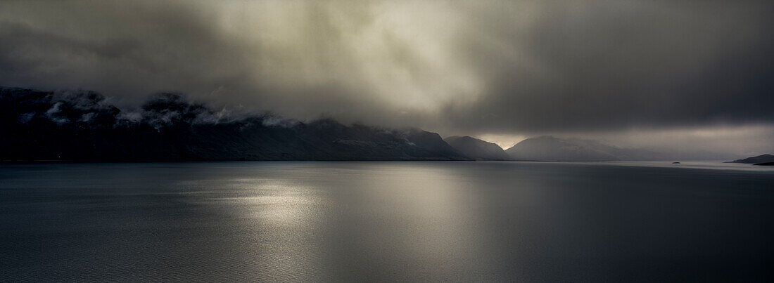 Panorama von Sonnenstrahlen, die durch Sturmwolken über The Remarkables und auf den Lake Wakatipu - Neuseeland scheinen