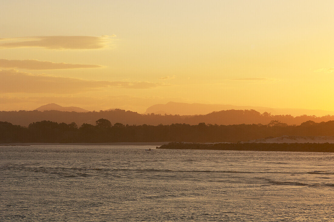 Flussmündung bei Sonnenuntergang mit einsamem Kyaker und Bergen im Hintergrund.