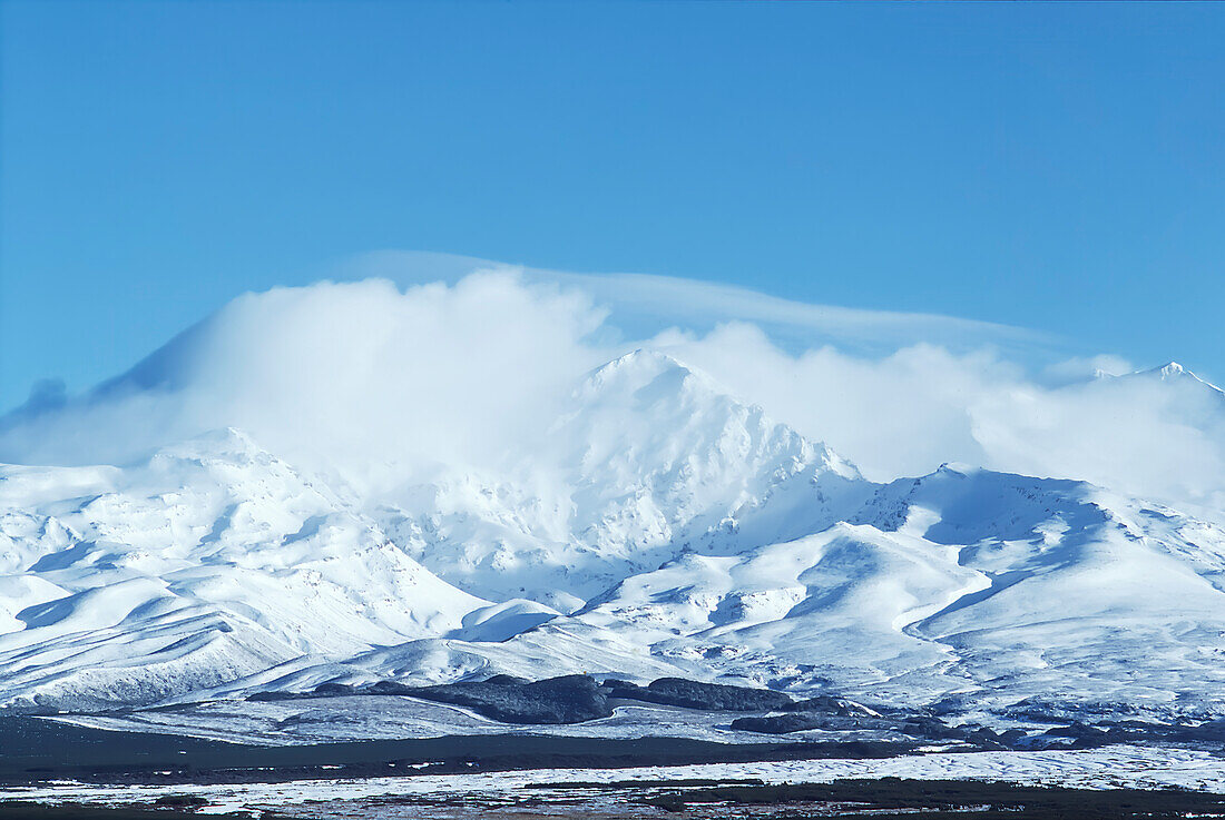 Snow covered Mount Ruapehu with shite cloud on top against blue sky