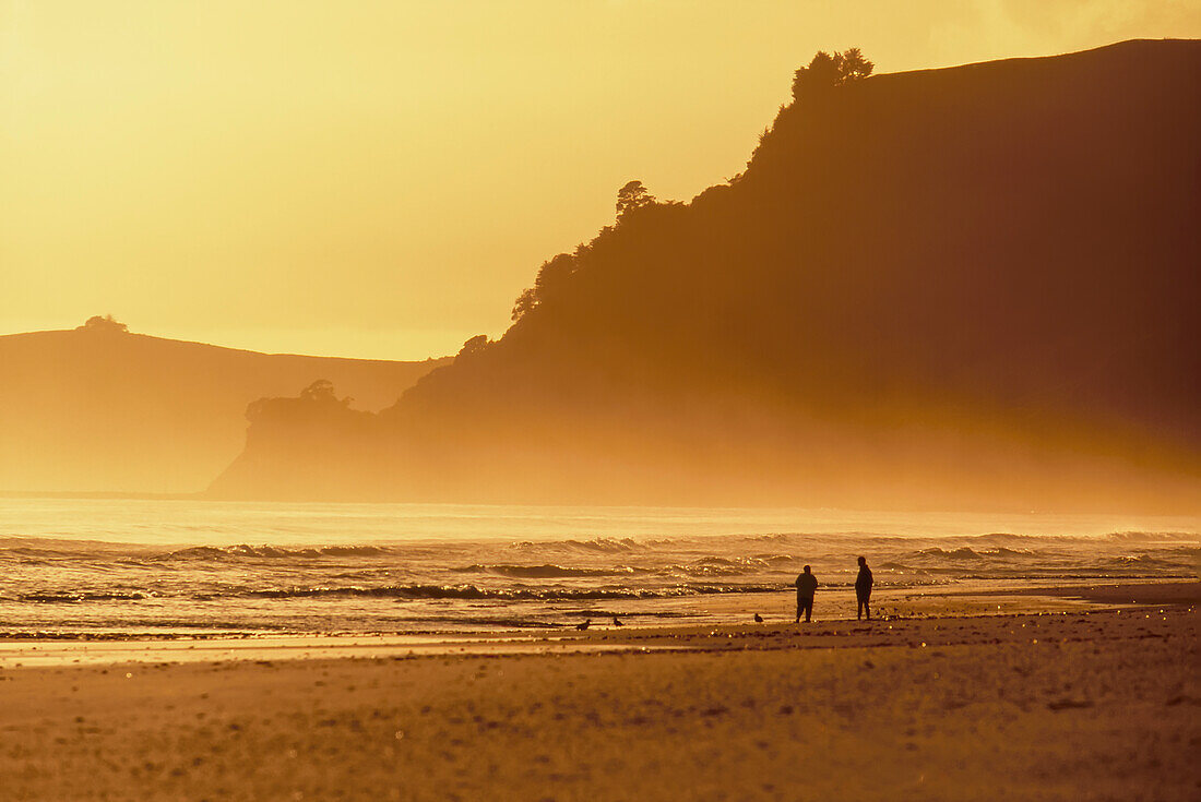 Zwei Personen genießen den Strand im goldenen Licht der Abenddämmerung