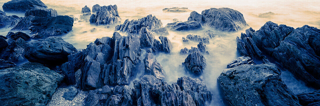 Misty waves rolling in around rocks on rocky beach