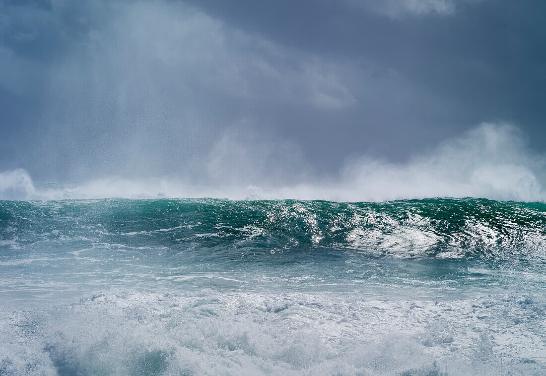 Welle kräuselt sich und bricht während des Zyklons Ola mit stürmischem Himmel