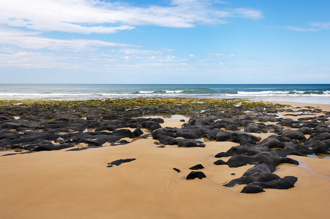 Gentle wave lapping onto smooth rocks on the beach at Fraser Island