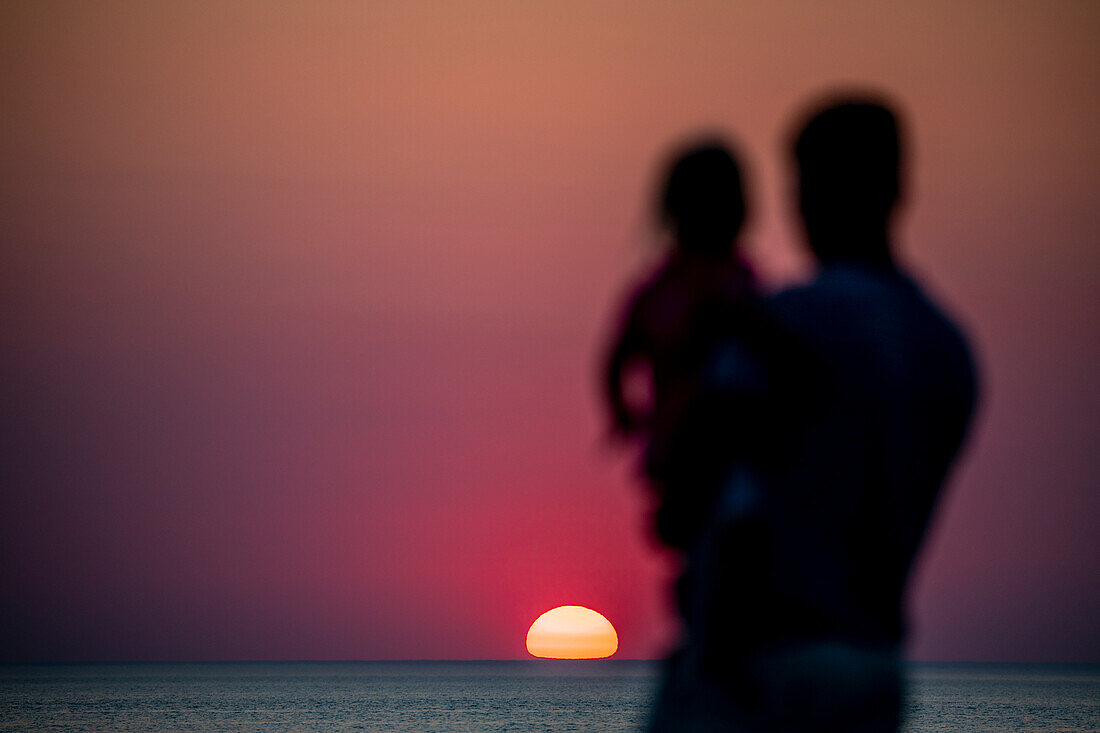 Mann mit Kind auf dem Arm blickt aufs Meer in Sonnenuntergang, Ostsee, Fischland-Darß-Zingst, Mecklenburg-Vorpommern, Deutschland