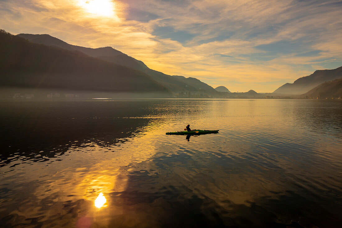 Frau in einem Kajak auf dem Luganersee mit Sonnenlicht und Berg im Tessin, Schweiz