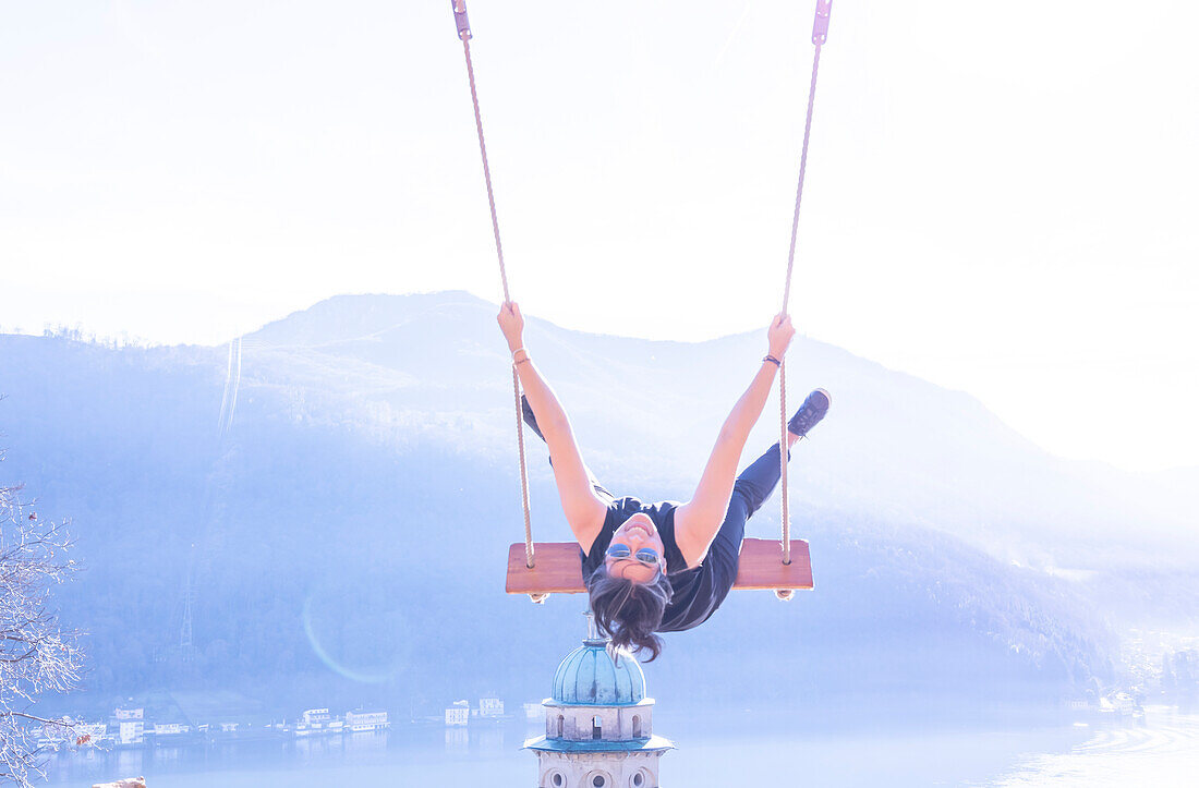 Woman on a Swing with Mountain View and Sunlight over Lake Lugano in Morcote, Ticino in Switzerland.