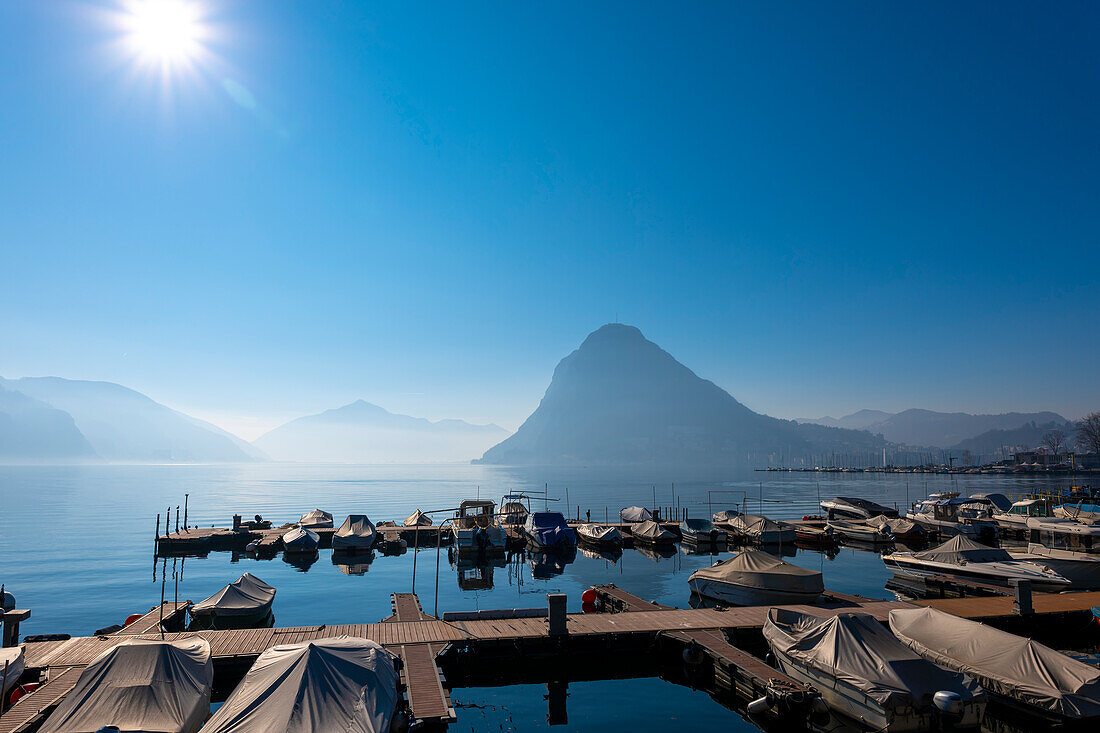 Port and Mountain Peak Monte San Salvatore in City of Lugano on Lake Lugano in a Misty Sunny Day in Ticino, Switzerland.