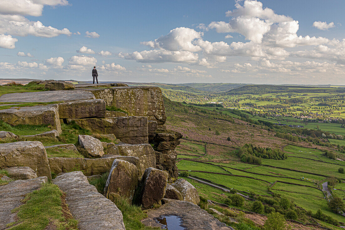 Person standing on cliff edge looking down valley at Curbar edge, Peak District, England, UK