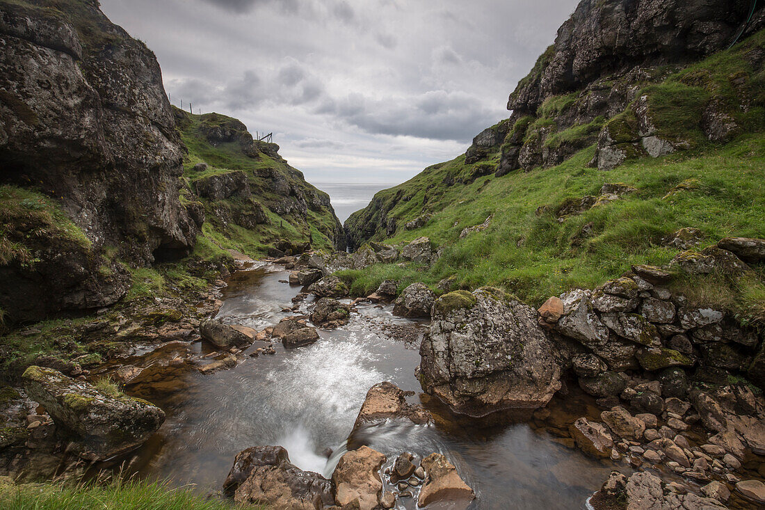 Stream running between mountains on coast, North Radalur, Streymoy, Faroe Islands.