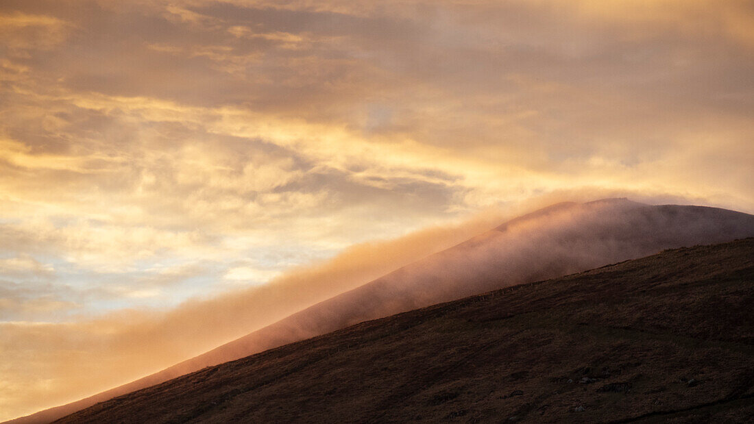 Wolken ziehen über Berg Cruach Mhartain zum Sonnenaufgang. Goldenes Licht. Clogher, Dnurlin, County Kerry, Irland.