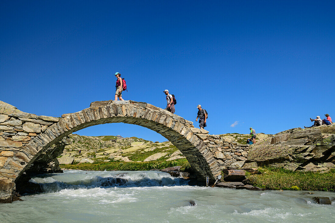 Drei Wanderer gehen auf Steinbrücke über Bergbach Reculaz, Nationalpark Vanoise, Vanoise, Savoyen, Frankreich