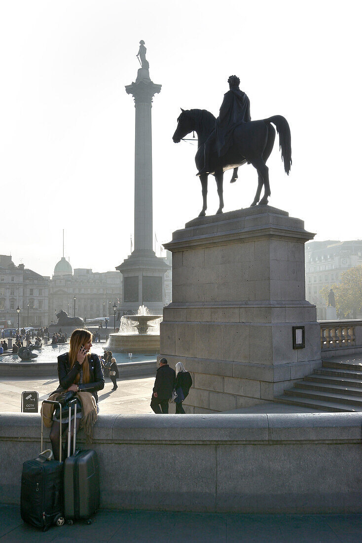 Girl on phone with suitcases, Trafalgar Square, London, UK