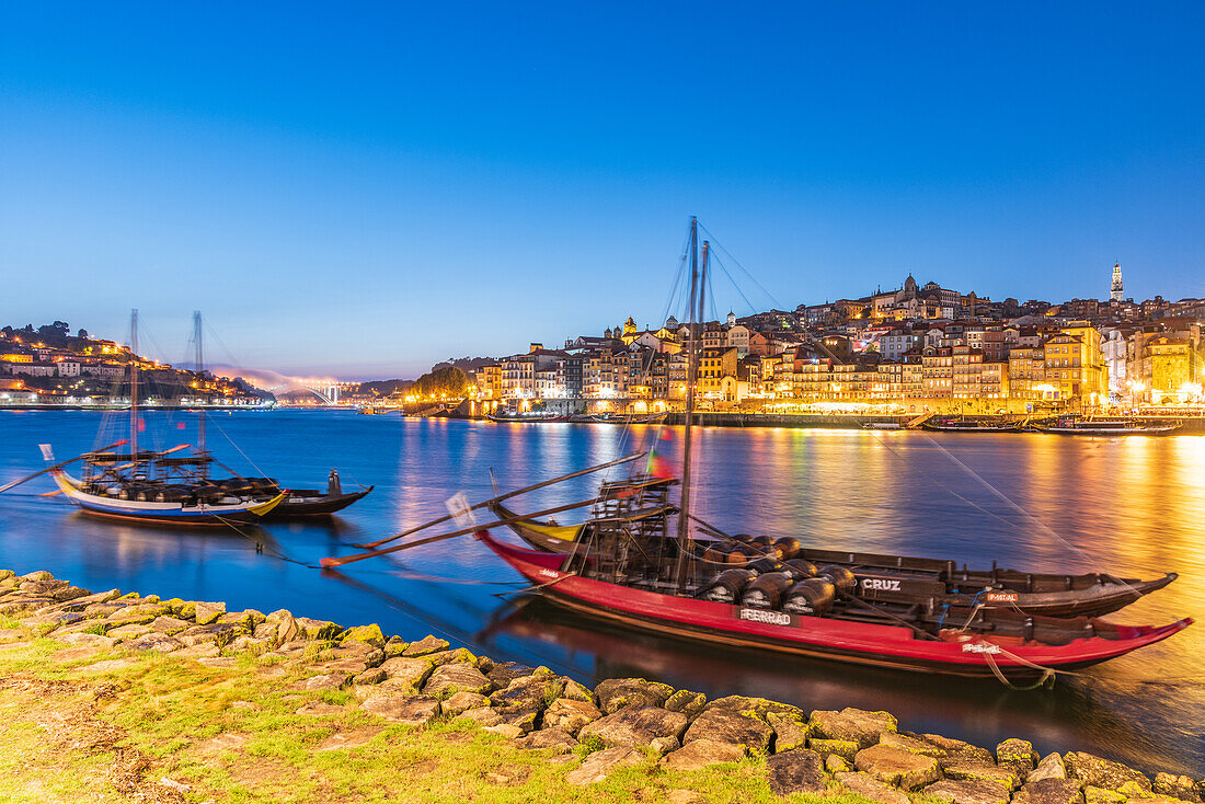 Barcos Rabelos, port wine boats on the Duero River in front of the historic old town of Porto at night, Portugal