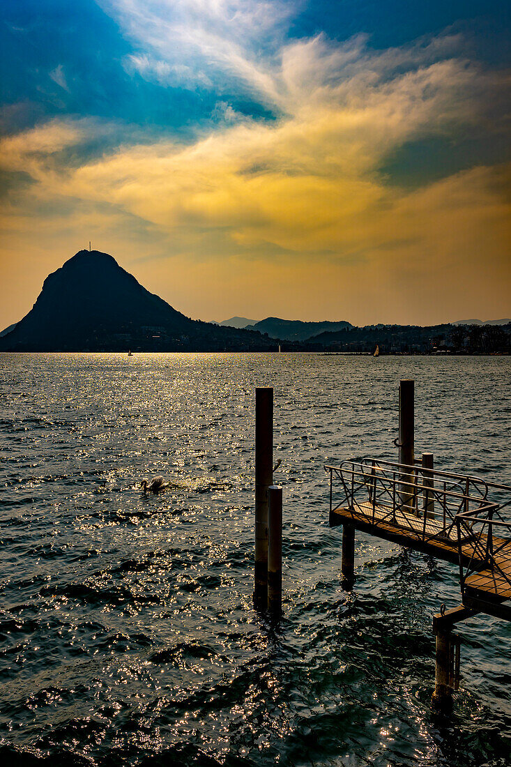 Mountain Peak Monte San Salvatore and a Jetty in City of Lugano and Lake Lugano in a Sunny Day in Ticino, Switzerland.