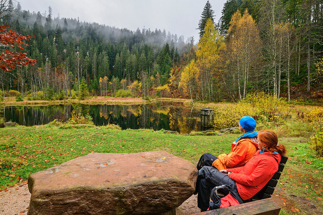 Mann und Frau beim Wandern sitzen am herbstlichen Ellbachsee, Ellbachsee, Nationalpark Schwarzwald, Schwarzwald, Baden-Württemberg, Deutschland