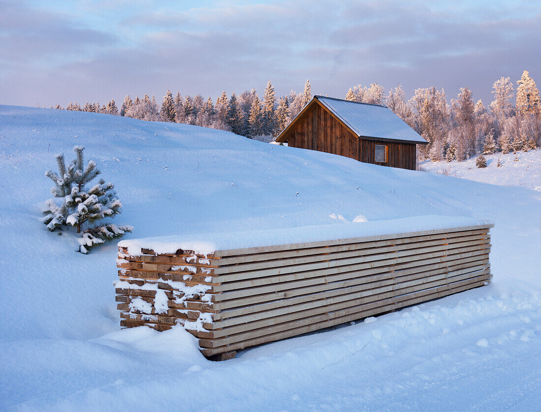 Stapelholz und kleines Holzhaus im Winterschnee