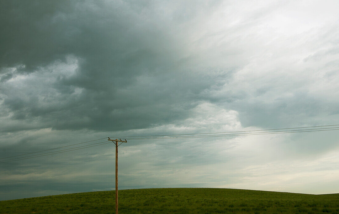 Power lines running through prairie and grassland with cloudy sky above.