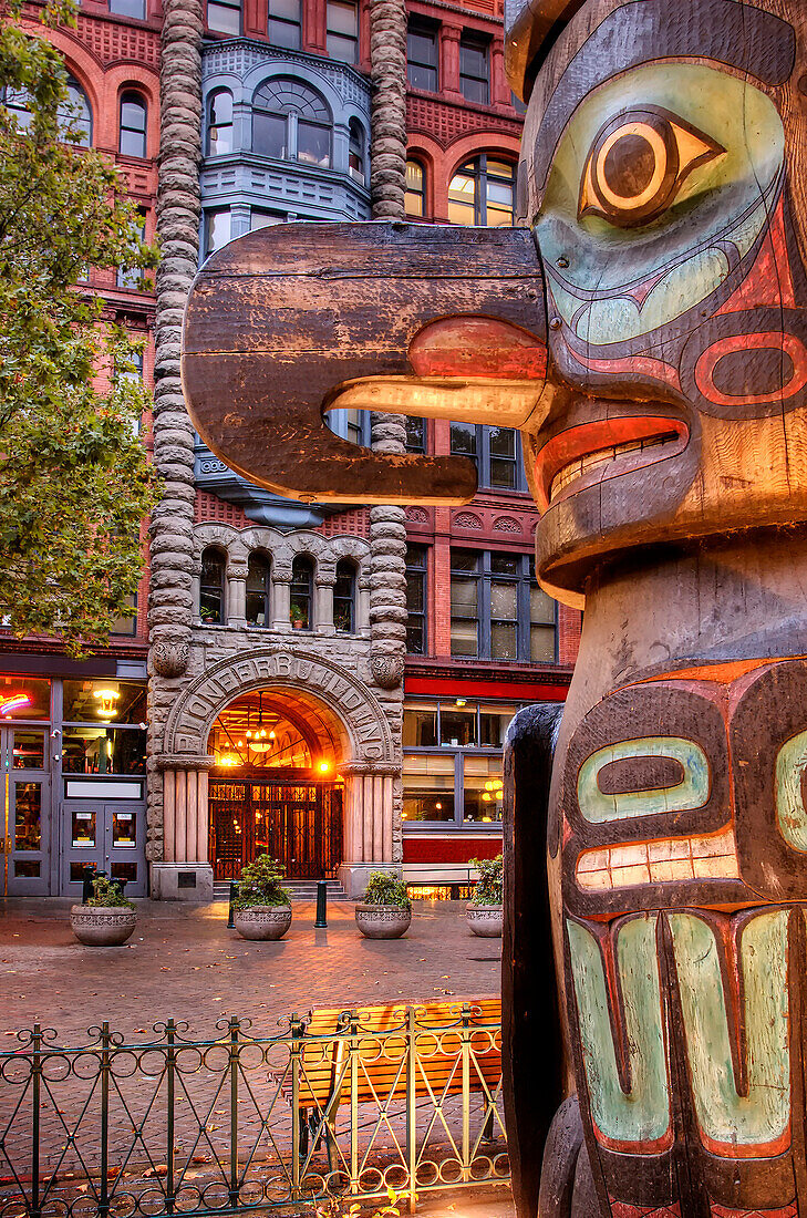 Totem pole on street with historic apartment building behind, Seattle, USA