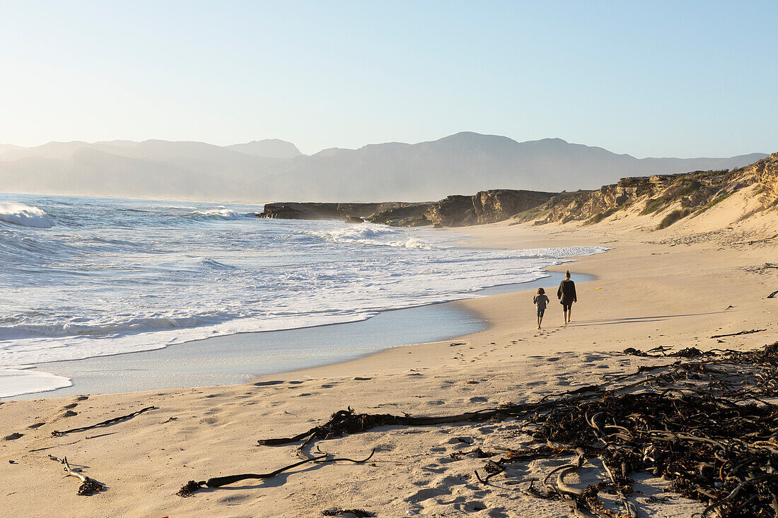 Zwei Menschen, die an einem Sandstrand spazieren, ein Teenager und ein Junge