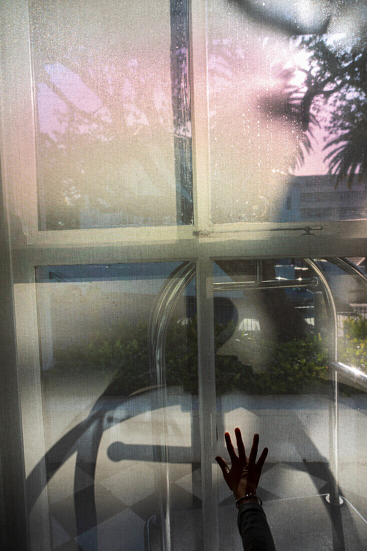 Child's hand, silhouette, pressed against a hotel window, reflections of foliage.