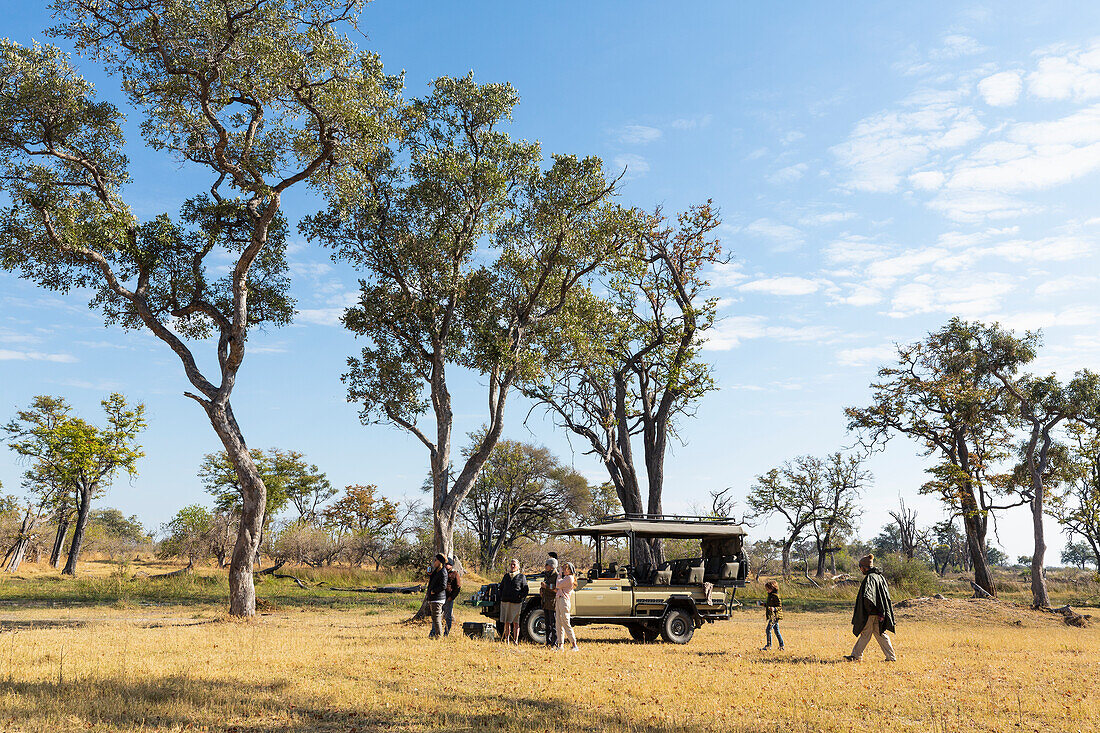 Ein Safarifahrzeug, das auf einer Wiese steht, und Menschen, die darum stehen, Okavango-Delta, Botswana, Afrika