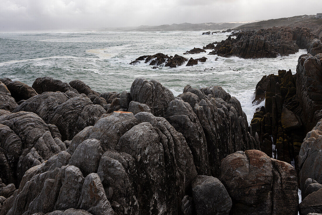 Jagged rocks and the rocky coastline of the Atlantic at De Kelders beach, waves breaking on shore, South Africa